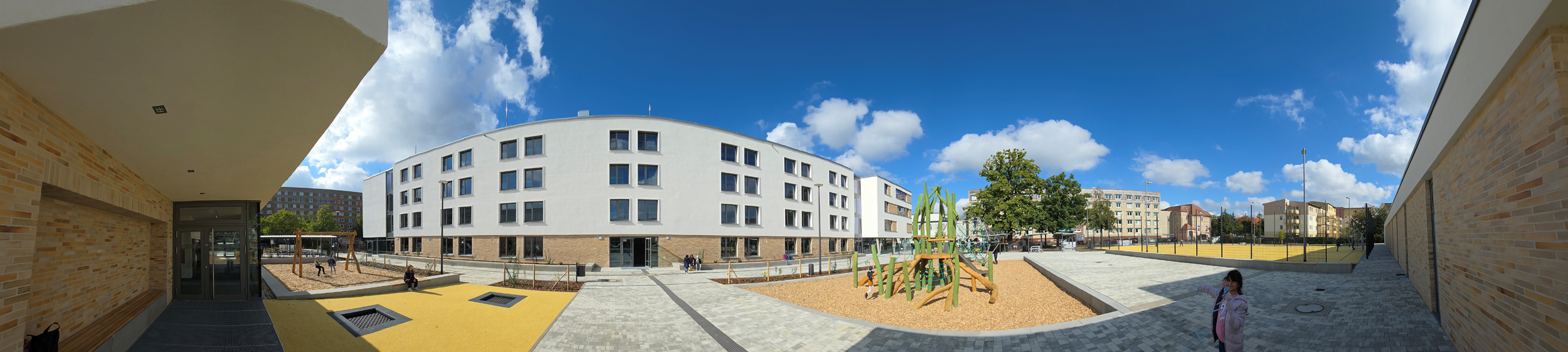 SPREEKIDS - Sprewanje Žiśi - Cottbus Standort Hallenserstraße Außenansicht SPREEKIDS - Sprewanje Žiśi - Cottbus Standort Hallenserstraße, Panoramablick auf den modernen Innenhof mit Spielplatz, umgeben von mehrstöckigen Wohngebäuden unter blauem Himmel mit Wolken